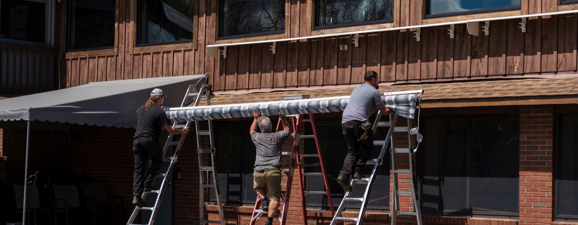 An installation crew on ladders mounting a retractable awning to a commercial building facade